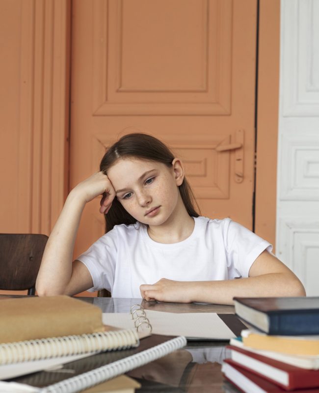 medium-shot-bored-girl-sitting-desk-with-books